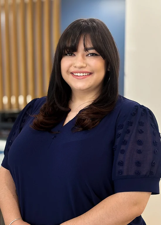 Woman with long dark hair and a navy blue blouse stands smiling, set against a bright, modern background.