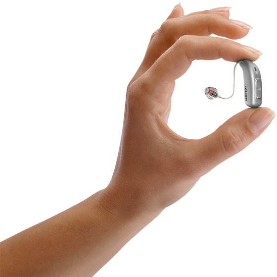 A woman’s hand holds a small silver-grey hearing aid between her fingers, showcasing its compact size.