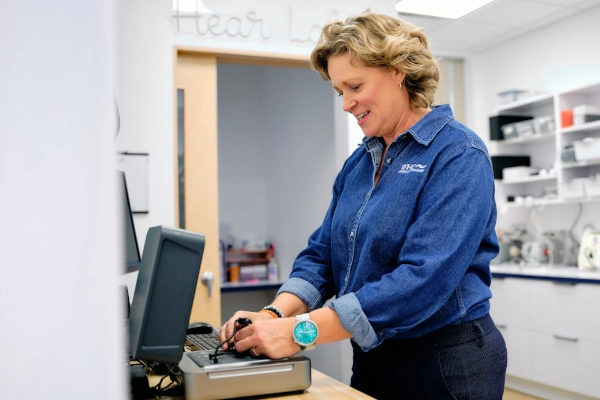 A woman in a denim shirt operates a computer at a work desk in a professional setting.