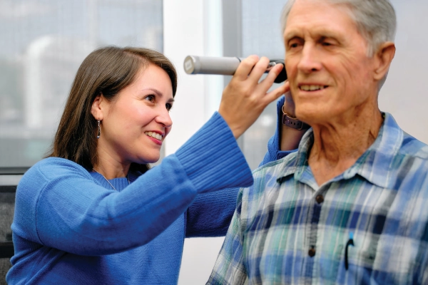 A healthcare professional conducts a hearing exam on an elderly man using an otoscope.