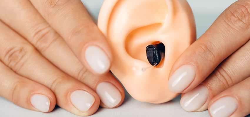 Hands holding fake ear with a hearing aid