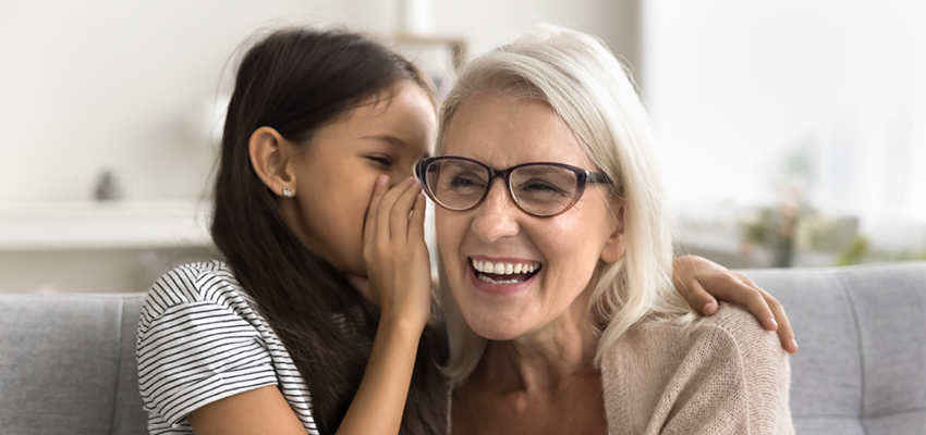 A child whispering into an older woman’s ear as they smile together, illustrating communication and connection through hearing