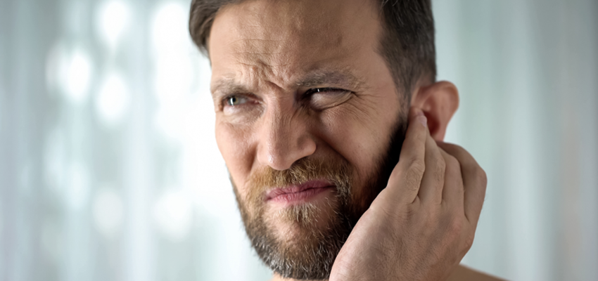 A man grimacing in pain and holding his hand to his ear, suggesting an earache or hearing discomfort